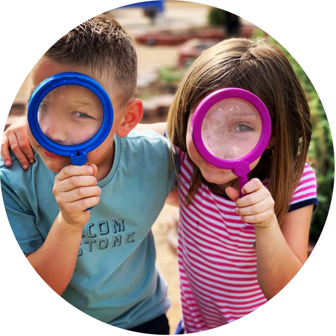 Two kids holding up colorful hand lenses to their faces, making their eyes look big